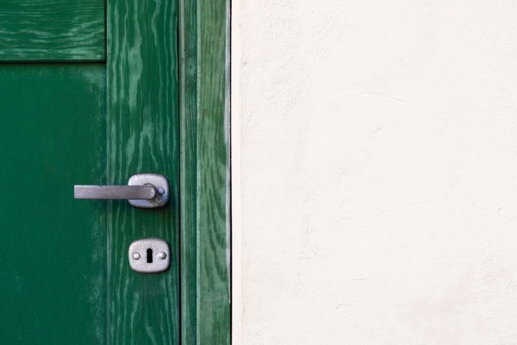 green wooden door beside white wall - housing help